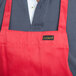 A person wearing a red Chef Revival apron with a front pocket.