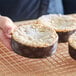 A hand holding a round brown and white Novacart Panettone baking mold filled with a cake.