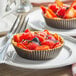 Two brown and white paper baking molds with fruit tarts on a plate.