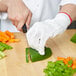 A person wearing a Mercer Culinary Millennia white cut-resistant glove cutting a green pepper.