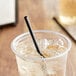 A close-up of a black EcoChoice PLA straw in a clear plastic cup with ice and liquid.