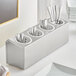 A stainless steel flatware organizer with white perforated plastic cylinders holding silverware.