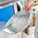 A person using a Choice aluminum flat bottom ice scoop to scoop ice into a metal container.