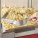 A hand holds a Choice aluminum flat bottom scoop filled with popcorn.