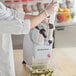 A person in a white coat and gloves using the AvaMix food processor to slice cucumbers.