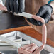 A person in black gloves cutting Backyard Pro Butcher Series sausage casing on a counter.