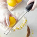 A hand using a Choice stainless steel zester to zest a lemon.