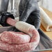 A person in a black glove wrapping Backyard Pro Butcher Series Collagen Sausage Casing around sausages on a tray.