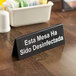 A Tablecraft black and white plastic sign that says "This Table Has Been Sanitized" in English and Spanish.