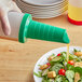 A person using a Tablecraft green PourMaster spout to pour salad dressing over a salad on a table.