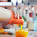 A hand using a Tablecraft PourMaster orange neck spout to pour orange liquid into a glass.
