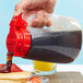 A person pouring syrup into a container using a Tablecraft 32 oz. Dispenser Jar with a red top.