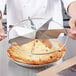 A chef using a Choice stainless steel pie cutter to slice a pie.