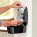 A person putting a plastic bag of hand soap into a black dispenser.