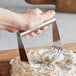 A hand using the Choice stainless steel pastry blender to cut dough over a pile of flour.