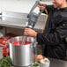 A man in a chef's jacket using a Hamilton Beach BigRig immersion blender to make soup in a professional kitchen.