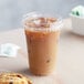 A clear plastic cup of iced coffee with a sip-through lid and a straw next to a cookie.