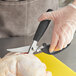 A person in a plastic glove using Choice 4" Stainless Steel Poultry Shears to cut chicken.