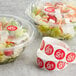 A salad in a plastic container with a red Point Plus label next to a roll of Point Plus red labels.
