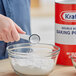 A close-up of a hand pouring Kraft baking powder into a bowl.
