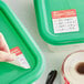 A hand using a Noble Products Wednesday label to mark a green container.