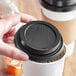 A hand holding a coffee cup with a black Choice hot cup lid on it.