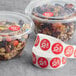 A roll of Point Plus red labels with food labels on plastic containers filled with nuts and dried fruit.