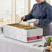 A woman in a chef's uniform using an Avantco countertop food warmer to serve food at a buffet.