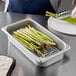 A person putting asparagus in a Vigor stainless steel steam table pan.