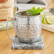 An Acopa silver Moscow Mule mug filled with ice and mint leaves on a marble coaster.