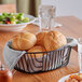 An Acopa black wire basket filled with rolls on a table.