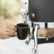 A hand using a Bon Chef stainless steel spigot adapter to fill a black coffee mug.
