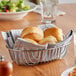 An Acopa oval chrome wire basket filled with rolls on a table.