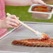 A person using a Backyard Pro BBQ brush mop to baste ribs on a grill.
