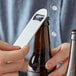 A hand using a Choice stainless steel bottle opener to open a brown bottle of beer.