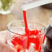 A person pouring Capora strawberry flavoring sauce into a glass of ice.