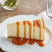 A slice of cheesecake on a plate with Capora Caramel Flavoring Sauce drizzled on top.