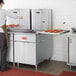 An aproned person using an Avantco gas fryer to cook donuts in a commercial kitchen.