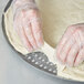 A person's hands in plastic gloves pressing pizza dough into an American Metalcraft Super Perforated Hard Coat Anodized Aluminum Pizza Pan.