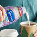 A hand pouring Splenda sugar-free sweet cream coffee creamer into a cup of coffee.