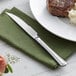 An Acopa stainless steel steak knife on a napkin next to a plate of food with a piece of meat.