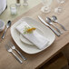 A table set with an Acopa Ridge stainless steel steak knife, spoon, and fork next to a plate with a flower on it.
