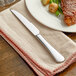 An Acopa Vernon stainless steel steak knife on a napkin next to a plate of food.