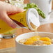 A hand pouring Domino brown sugar into a bowl of oranges on a table with a bowl of oatmeal.