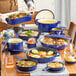 A table set with a Valor Galaxy Blue enameled cast iron skillet and other blue enameled cast iron cookware filled with various foods.