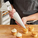 A person using a Choice 18" plastic coated canvas pastry bag to frost cupcakes.