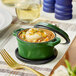 A Valor fern green enameled cast iron pot with a lid on top of a table with food in it.