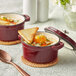 Two Valor merlot enameled cast iron pots with soup and toast on a white table.