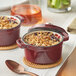 A red Valor Merlot enameled cast iron pot with food in it on a table with a spoon and a bowl of food.