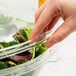 A hand putting a dome lid on a Fineline plastic bowl of salad